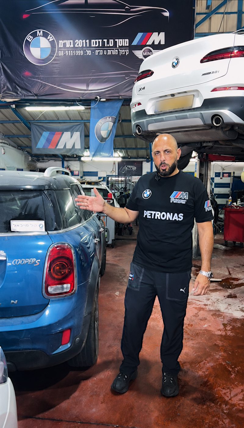 בעל מוסך בתוך הסדנה, לצד רכבי BMW ו-MINI בטיפול